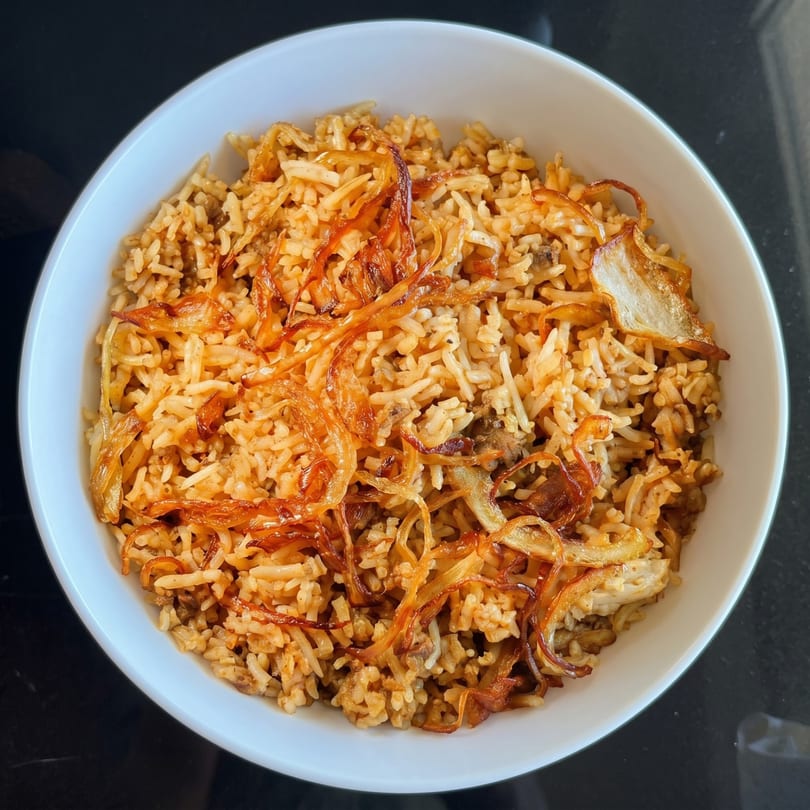 A white bowl filled with biryani rice and topped with crispy fried onions.
