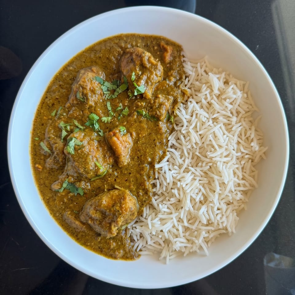 A white bowl filled with green curry chicken and white basmati rice, garnished with cilantro.