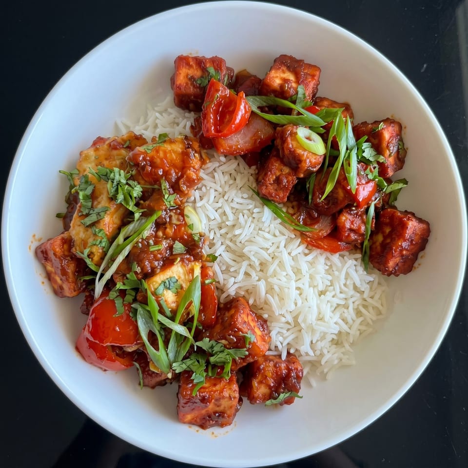 A white bowl filled with basmati rice, chili paneer, bell peppers, and garnished with green onions.
