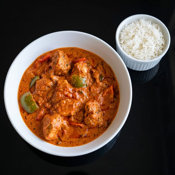 Chicken tikka masala with green peppers in a white bowl, served with a side of white rice.
