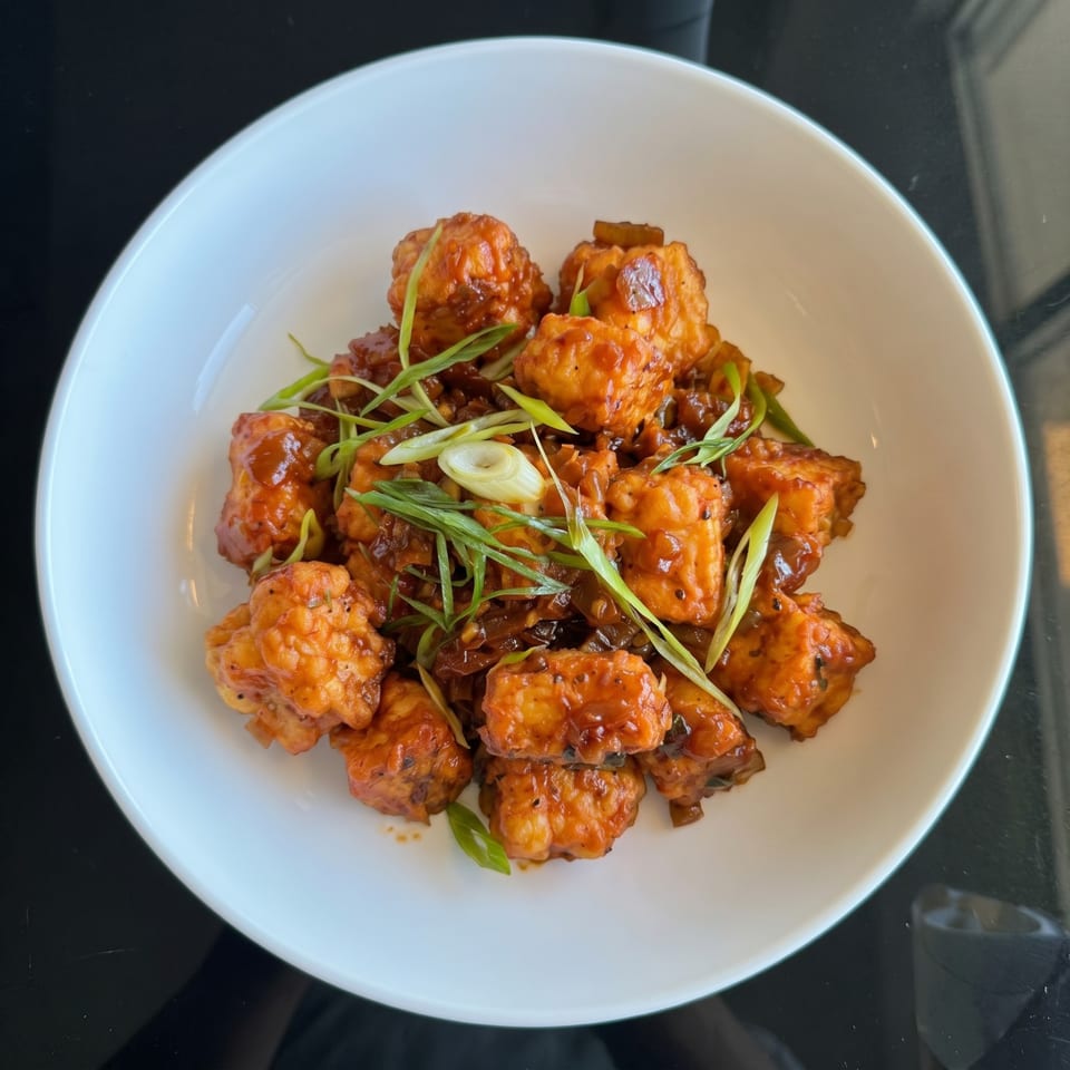 Crispy orange chicken pieces coated in a glossy sauce, garnished with fresh green onions in a white bowl.