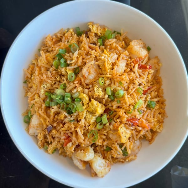 Shrimp fried rice with scrambled egg, red peppers, and green onions in a white bowl.