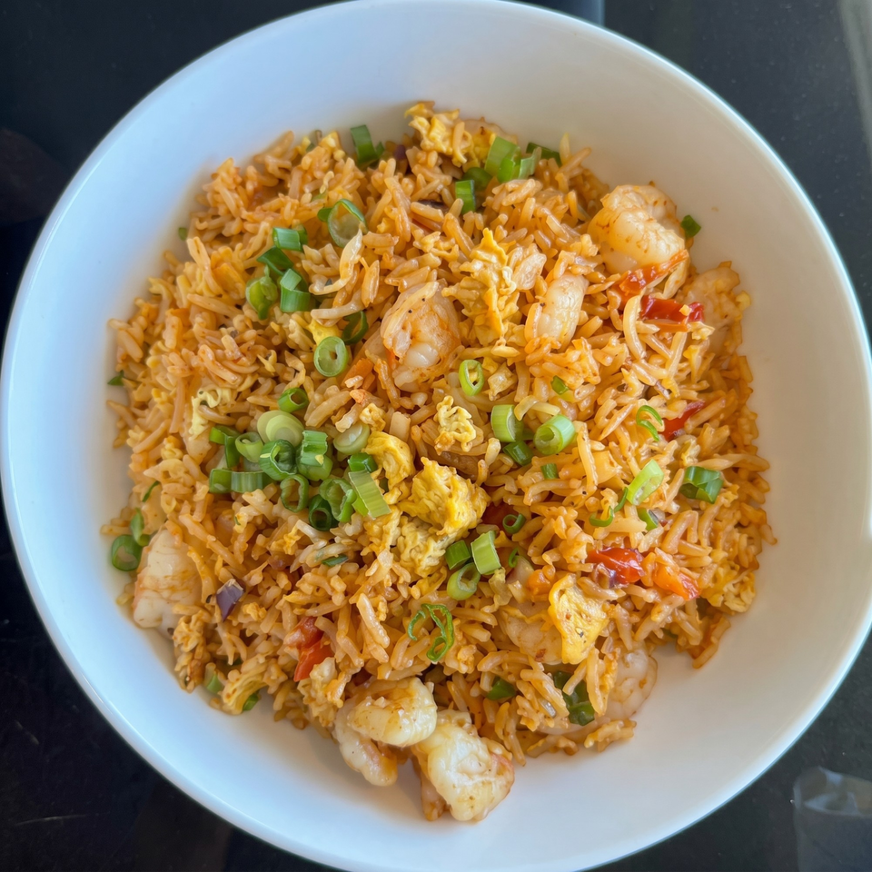 Shrimp fried rice with scrambled egg, red peppers, and green onions in a white bowl.