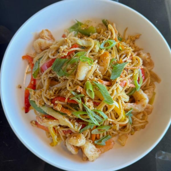 A white bowl filled with shrimp lo mein, colorful vegetables, and green onions.